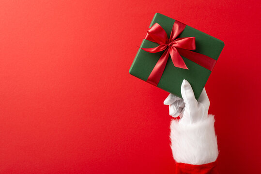 Close-up of Santa Claus hand holding a green gift with a red ribbon, symbolizing Christmas and festive cheer