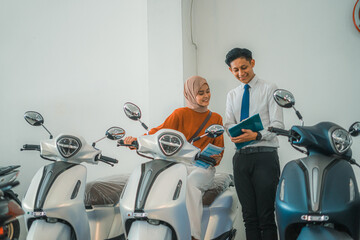 female customer riding a motorcycle looking at the price list with a male salesperson at a showroom