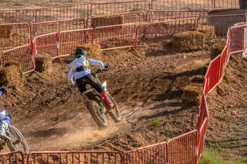 Motocross riders cornering standing up on their bikes racing on a muddy track during an outdoor...