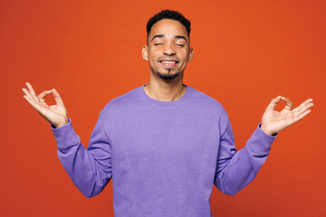 Fototapeta premium Young man he wears purple sweatshirt casual clothes hold spreading hands in yoga om aum gesture relax meditate try to calm down close eyes isolated on plain red orange background. Lifestyle concept.