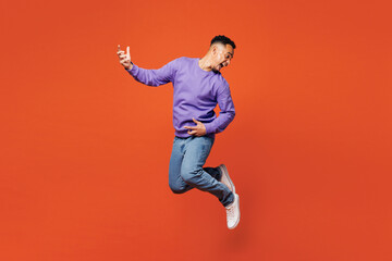 Full body side view young happy man of African American ethnicity he wear purple sweatshirt casual clothes jump high play air guitar isolated on plain red orange background studio. Lifestyle concept.