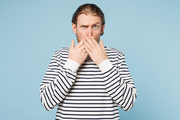 Young sad shocked surprised unhappy man he wear striped sweatshirt casual clothes look camera put hand on mouth isolated on plain pastel light blue cyan background studio portrait. Lifestyle concept.