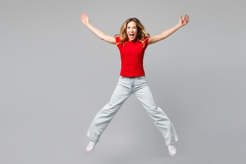 Full body young smiling excited happy woman she wear red t-shirt casual clothes jump high look camera with outstretched hands legs isolated on plain grey background studio portrait. Lifestyle concept.