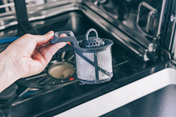 Man cleans the filter in the dishwasher. Maintenance of home appliances.
