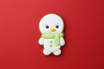 Tasty Christmas cookie in shape of snowman on red background, top view