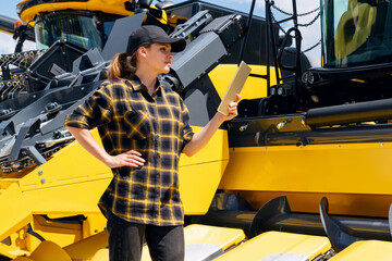 A woman using a digital tablet stands next to a yellow combine harvester at a farm equipment dealership.