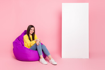 Full length photo of young cheerful girl sit violet beanbag promoter isolated over pink color background