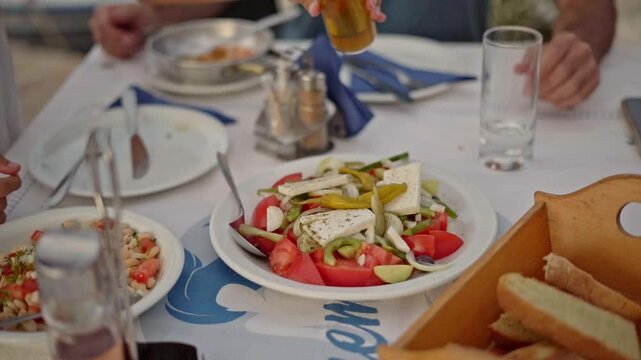 People at beach cafe eating traditional mediterranean salad seasoning with olive oil at Greek taverna, Closeup