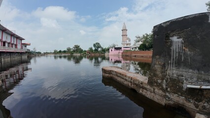 Tranquil pond in a village, showcasing a temple complex, embodying calmness and serving as a sacred pilgrimage destination. Haryana, India 