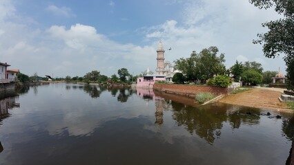 Tranquil pond in a village, showcasing a temple complex, embodying calmness and serving as a sacred pilgrimage destination. Haryana, India 