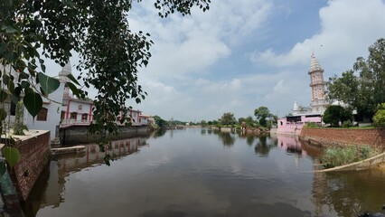 Obraz premium Tranquil pond in a village, showcasing a temple complex, embodying calmness and serving as a sacred pilgrimage destination. Haryana, India 