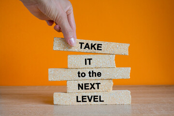 Brick blocks with the message take it to the next level. Businessman hand. Beautiful wooden table orange background. Business career path for growth and success concept.