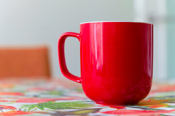 A red coffee cup sits on a table with a colorful tablecloth
