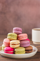 Multicolored macarons in a plate with cup of coffee on a wooden table. Vertical orientation.