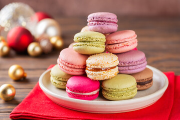 Multicolored macaroons in a plate with Christmas balls on a red napkin. Christmas background.