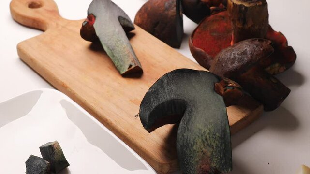 Wild forest mushrooms, olive brown bolete and speckled boletus, on a wooden board. Cross-section of a blue-colored mushroom, slicing mushrooms with a sharp knife on a cutting board