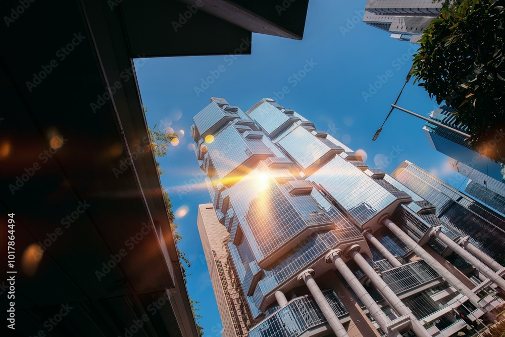 Wall mural A low angle view of a tall, modern office building in Hong Kong, bathed in sunlight.