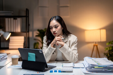 Young asian businesswoman working late using digital tablet in office at night