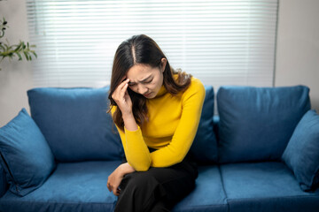 Obraz premium Young asian woman feeling sick and having a headache while sitting on the sofa at home