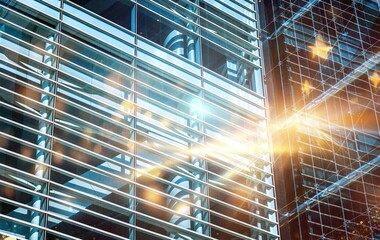 A modern skyscraper with a grid of glass windows, with a bright sun shining through.