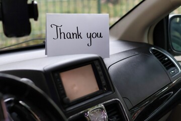 A white card with a handwritten inscription "thank you" on the dashboard of a car