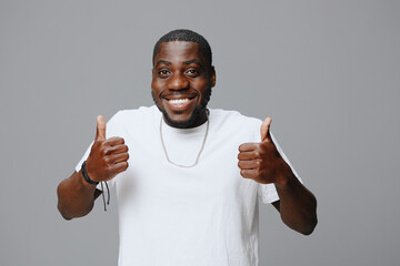 Happy young man giving thumbs up, wearing a white t shirt, expressing joy and positivity, against a...