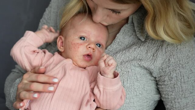 Close up mother gently stroking belly and kissing 1 month old baby, dressed in light pink clothing. Tender loving connection between mom and child, warmth, care and affection in peaceful