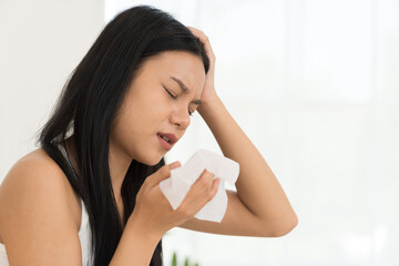 Young Asian woman feeling unwell and have a headache while sitting on the bed. Young woman have symptoms of illness and holding her head