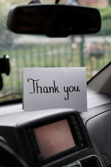 A white card with a handwritten inscription "thank you" on the dashboard of a car © Gosia