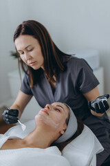 Cosmetologist performs a facial peeling procedure on a young woman.