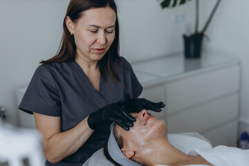 Cosmetologist performs a facial peeling procedure on a young woman.