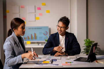 Two people are sitting at a desk with a lot of papers and graphs © apichat