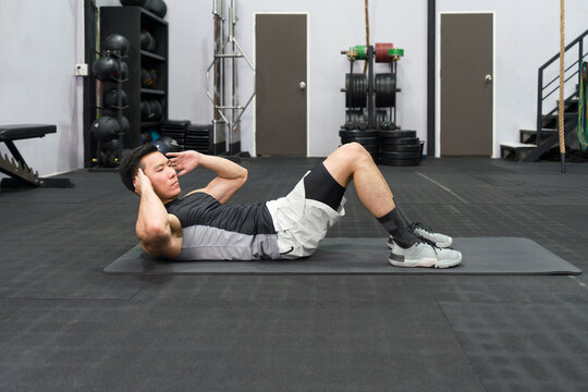 Young asian man Sit-up on exercise mat. There are dumbbell set with rack in the gym.