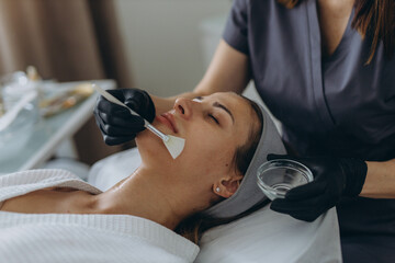 Cosmetologist performs a facial peeling procedure on a young woman.