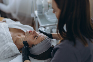 Cosmetologist performs a facial peeling procedure on a young woman.