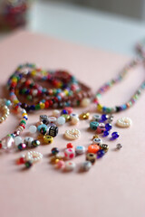 Colorful DIY necklaces, friendship bracelets and various plastic beads on pastel pink background. Selective focus.