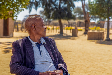 Fototapeta premium african village , happy single old man sited on a chair in the yard in front of the house