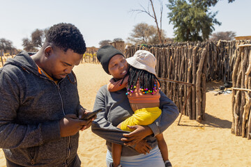 african village , social worker volunteer using phone teaching wireless technologies to villagers, mother and daughter with braids , outdoors kitchen, wooden fence,