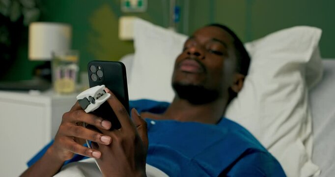 African patient relaxed on the bed, engaged in texting on his phone, keeping loved ones informed about his well-being.