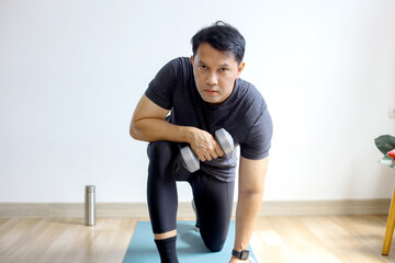 Fototapeta premium Portrait of Asian sporty man doing dumbbells workout at home, working on arms strength.