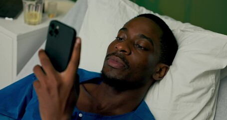Guy in the hospital bed, holding his phone for a video call, talking to his family or friends to stay connected and feel better.