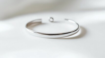 A simple silver bangle bracelet sits on a white surface.
