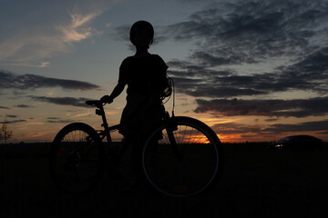Obraz premium Silhouette of a cyclist standing beside their bike at sunset, capturing the peacefulness of dusk in the countryside. High quality photo