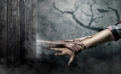 A zombie hand with a bloody wound grabs a human hand in dark room. Scene has dark and scary....
