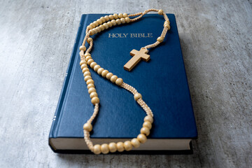 Wooden religion cross on rosary beads and blue book with the word Holy Bible. It is laying on a wooden table. Religious christian holiday. Symbol of faith in God, Christianity Feast