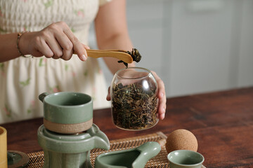 Close-up of woman putting dry herbs in tea pot, she making herbal tea in the kitchen