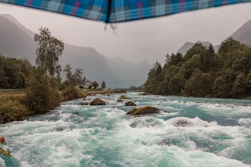A rushing river cuts through a lush green valley, framed by towering mountains and an umbrella....