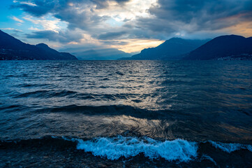 Panorama of Lake Como, in Dervio, with sailing boats and the sun's rays illuminating the lake.