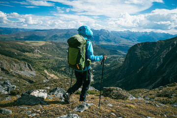Fototapeta premium Backpacking woman climbing up on steep cliff edge at high altitude mountains top