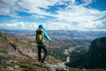 Fototapeta premium Backpacking woman climbing up on steep cliff edge at high altitude mountains top